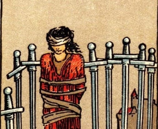 A figure stands blindfolded and bound up with 8 swords around them pointed into the ground. A castle is in the background.